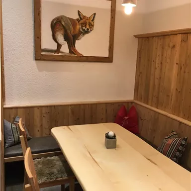 Ein gemütlicher Essbereich mit einem großen Holztisch und Bänken. An der Wand hängt ein Gemälde eines Fuchses.