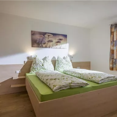 Ein gemütliches Schlafzimmer mit zwei Einzelbetten und grünem Bettzeug. Das Zimmer hat natürliche Holzdetails und ein Fenster mit Vorhängen.