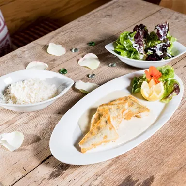 A delicious dish with a fish fillet in sauce, served with fresh salad and a slice of lemon. On the side, there is a small bowl of rice.
