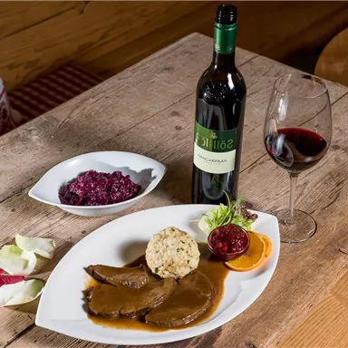 A delicious dish with tender meat, side dishes, and a serving of cranberries. Next to it stands a bottle of red wine and a glass.
