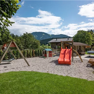 A beautiful playground in a green environment. There are swings, slides, and a magnificent view of the mountains.