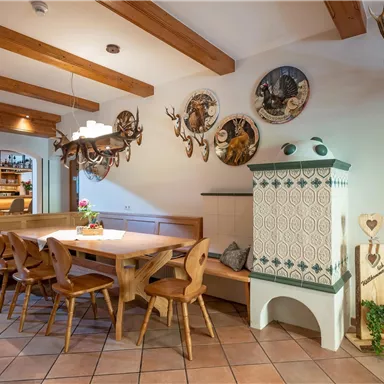 A cozy dining area with a large table and wooden benches. Decorative trophies hang on the walls, and a traditional stove stands in the corner.