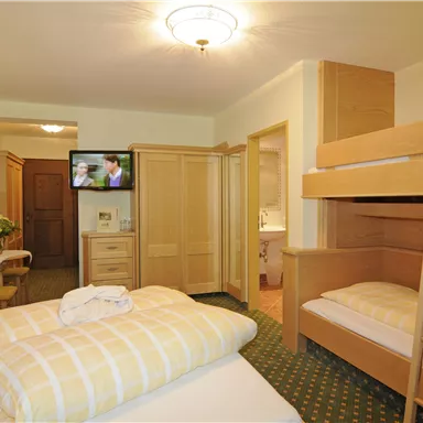 A cozy hotel room with a double bed and a bunk bed. In the background, a television and a desk can be seen.
