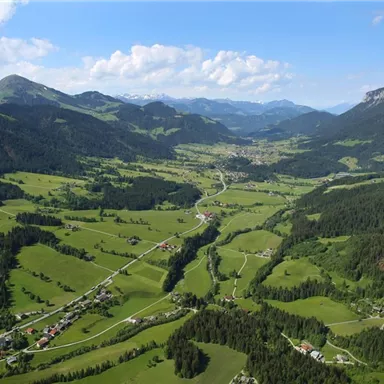 A picturesque landscape with gentle hills and green meadows. The mountains form an impressive backdrop in the background.