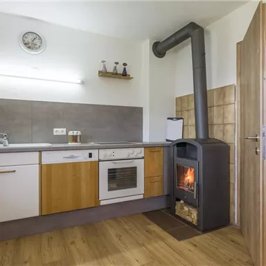 Eine moderne Küche mit Holzfußboden und einer Kochzeile. Ein Ofen steht in der Ecke und gibt Wärme ab.