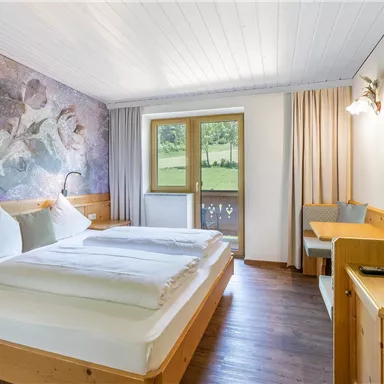 Ein Schlafzimmer mit zwei Einzelbetten, Holzmöbeln und einem Fenster, das auf eine grüne Landschaft blickt. Die Wände sind mit einer bunten Tapete dekoriert, die einen modernen Akzent setzt.