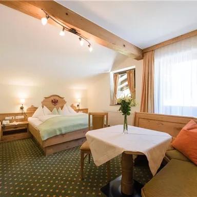 A cozy hotel room with two beds and a table. The windows are bright, and a bouquet decorates the table.