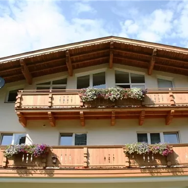 Ein alpin inspirierte Fassade mit Holzbalkonen und bunten Blumen. Der Himmel ist klar und blau.