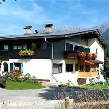 Ein gemütliches Ferienhaus mit Blumenbalkonen und einer schönen Landschaft im Hintergrund. Die Umgebung ist grün und lädt zum Entspannen ein.