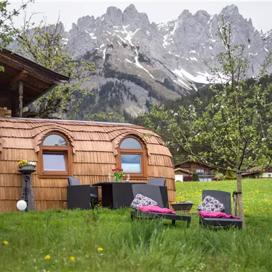 Ein gemütliches Holzhaus in einer malerischen Landschaft. Im Hintergrund sind majestätische Berge mit Schnee zu sehen.