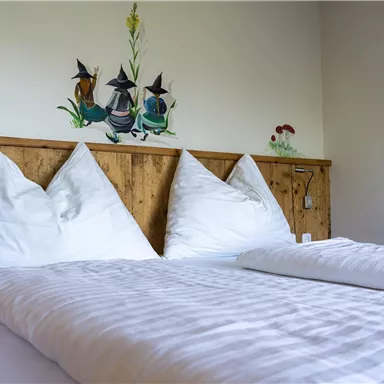 A cozy bedroom with a wooden bed and two white pillows. There is a decorative painting on the wall.