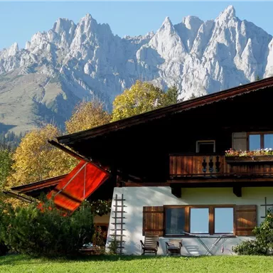 A picturesque chalet in front of imposing mountain peaks. The surroundings are green and inviting, ideal for a retreat in nature.