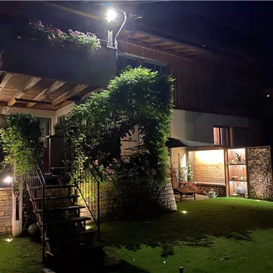Ein schön beleuchtetes Haus mit einem begrünten Garten. Die Pflanzen und Lichter sorgen für eine gemütliche Atmosphäre in der Nacht.