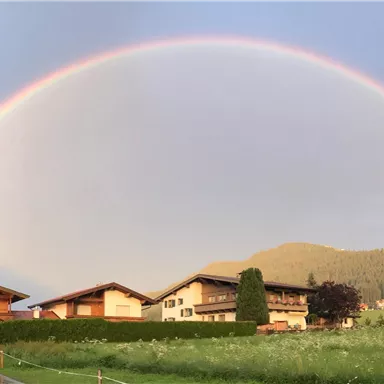 A beautiful rainbow stretches over picturesque houses and green meadows. The landscape is peaceful and invites admiration.