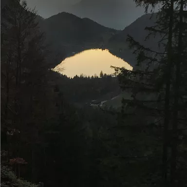 A picturesque mountain landscape at sunset. A calm lake reflects the colors of the sky, surrounded by forests.