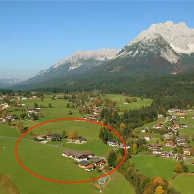 A picturesque landscape with green meadows and scattered houses. In the background, majestic mountains can be seen touching the sky.