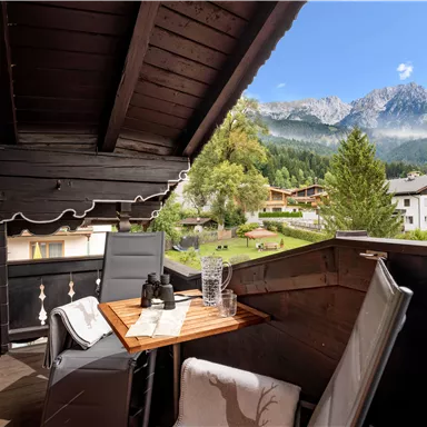 Ein gemütlicher Balkon mit einem Tisch und Stühlen bietet einen schönen Blick auf die Berge und die umliegende Landschaft. Die Sonne scheint und es ist eine friedliche Atmosphäre.