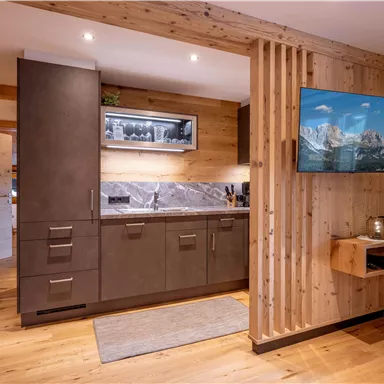 Eine moderne Küche mit Holzverkleidung und stilvollen Geräten. Ein Fernseher zeigt eine Berglandschaft an der Wand.