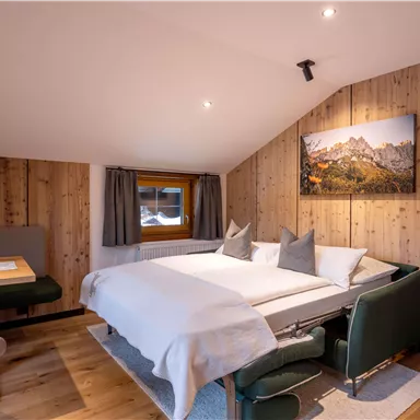 Ein gemütliches Schlafzimmer mit Holzvertäfelung und einem Doppelbett. Es gibt einen kleinen Essbereich und ein Fenster mit Blick auf die Berge.
