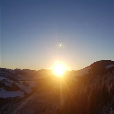 Eine atemberaubende Aussicht auf einen Sonnenaufgang über den verschneiten Bergen. Die Sonne strahlt über die Landschaft und schafft eine warme, goldene Atmosphäre.