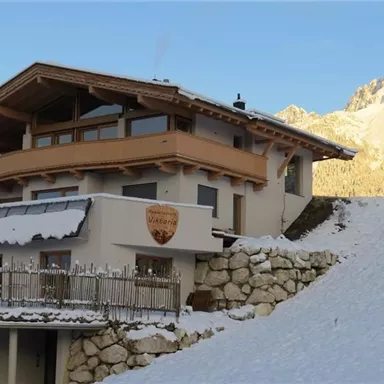Ein modernes Chalet inmitten von Schnee und Bergen. Die majestätischen Felsen im Hintergrund verleihen der Szene eine malerische Atmosphäre.