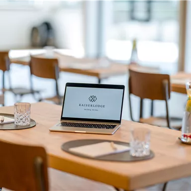 Ein moderner Tisch in einem Restaurant mit einem Laptop und Trinkgläsern. Der Raum ist hell und einladend gestaltet.