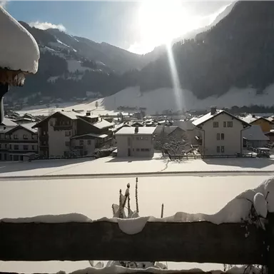A snowy landscape with houses and mountains in the background. The sun is shining and illuminating the scene.