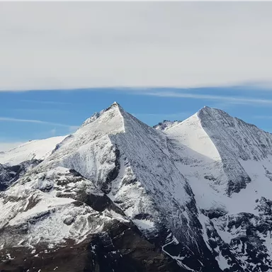 Ein majestätisches Bergpanorama mit schneebedeckten Gipfeln. Der Himmel ist klar und blau, was die Schönheit der Natur unterstreicht.