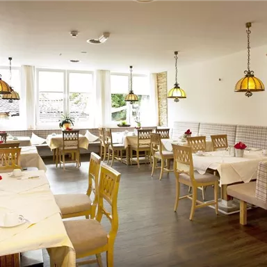 Ein helles Restaurant mit eleganten Holzstühlen und Tischen. Die warmen Lampen sorgen für eine gemütliche Atmosphäre.