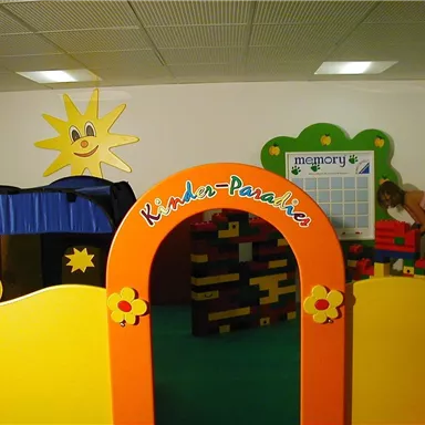 A colorful play area with an arch that says "Children's Paradise." In the background, there is a sun and various play stations visible.