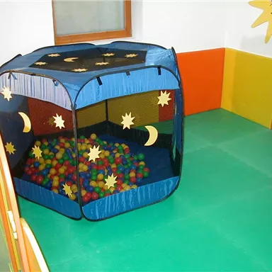 A play tent with colorful balls in a vibrant playroom. The walls are designed in bright colors, and there is a large window area.