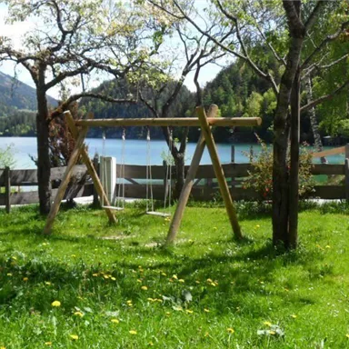 Ein schöner Spielplatz mit einer Schaukel und einem Tunnel. Im Hintergrund ist ein See und grüne Wiesen zu sehen.