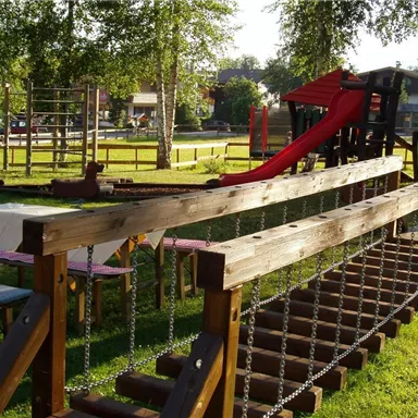 A playground with a slide and a climbing frame in a green park landscape. Tables are ready for visitors who want to enjoy nature.