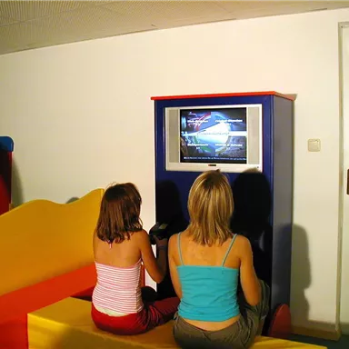 Two girls are sitting on a colorful bench and watching television. The room has a modern and inviting design.