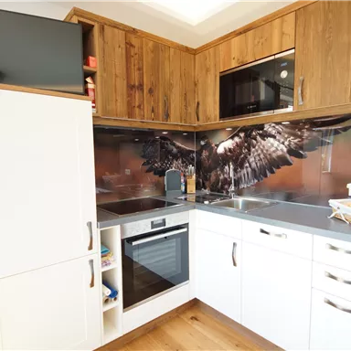 A modern kitchen with wood surfaces and gray countertops. In the background, there is an impressive wall design featuring an eagle.