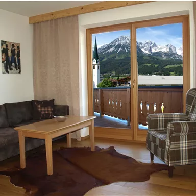 A cozy living room with a sofa and an armchair. Large windows provide a view of the mountains.