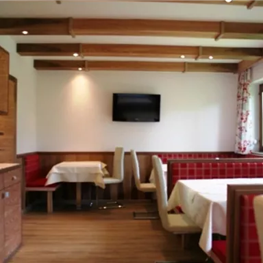 A cozy dining room with wooden paneling and red benches. A TV hangs on the wall and large windows let in plenty of light.