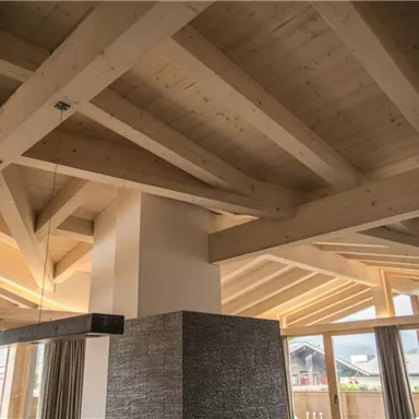 Ein modernes Rauminterieur mit Holzdecken und großen Fenstern. Das Licht strömt durch die Fenster und schafft eine einladende Atmosphäre.