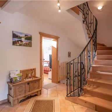 Ein einladender Flur mit einer Holztreppe und schönen dekorativen Elementen. Helle Wände und viele Türen sorgen für eine gemütliche Atmosphäre.
