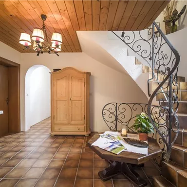 Ein einladender Flur mit einer eleganten Wendeltreppe und einem Holzmobiliar. Der Raum hat eine warme Atmosphäre mit Holzdecken und gefliesten Böden.