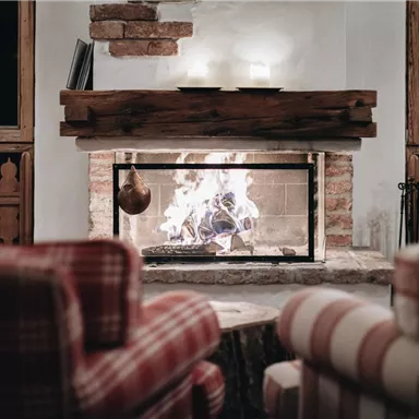 A cozy fireplace with a flaming fire in a rustic room. The comfortable armchairs create an inviting atmosphere.