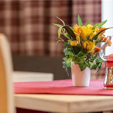 A beautifully decorated table with a flower pot and a glass vase. In the background, checkered curtains are visible.