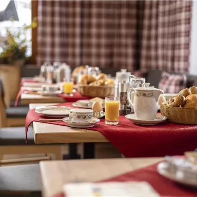 A beautifully decorated breakfast table with rolls, cheese, and a jug of juice. The surroundings are warm and inviting, perfect for a cozy start to the day.