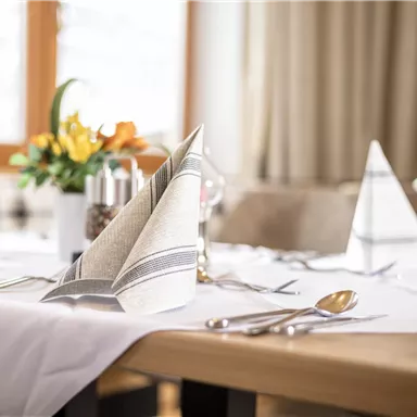 A beautifully set table with elegant napkins and cutlery. In the background, fresh floral arrangements can be seen.