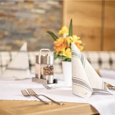 A stylishly set table with fine napkins and cutlery. A blooming plant in a vase complements the elegant table decoration.