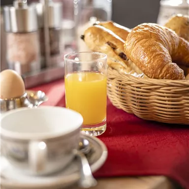 A set breakfast table with croissants, a boiled egg, and a glass of orange juice. In the background, salt and sugar containers are visible.