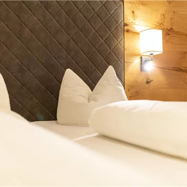 A cozy bedroom with a bright bed and decorative pillows. The walls are warm and a soft light creates an inviting atmosphere.