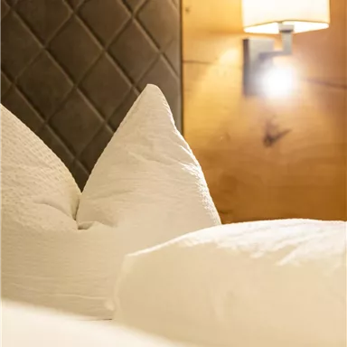 A cozy bedroom with white pillows and soft wall lighting. The wooden paneling creates a warm atmosphere.