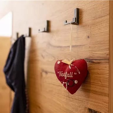 A wooden wall hook with a red heart as decoration. The heart bears the inscription "Emergency".