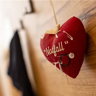 A red heart hangs on the wall and carries the word "Emergency". It is decorated with a safety pin and a thread.